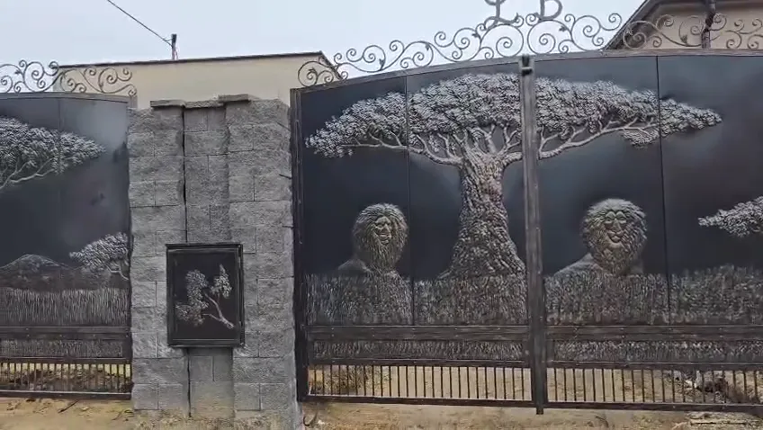 Brama z kutym ornamentem, drzewem i portretami oraz ogrodzenie z drzewami